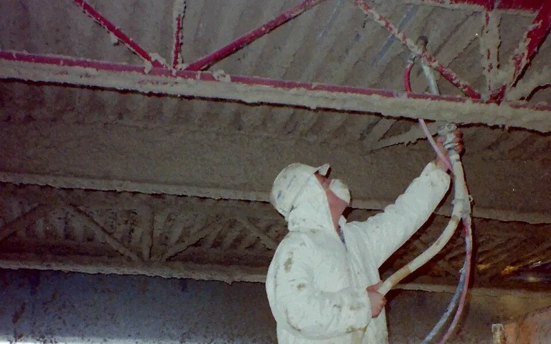 Worker applying spray fireproofing to structural steel