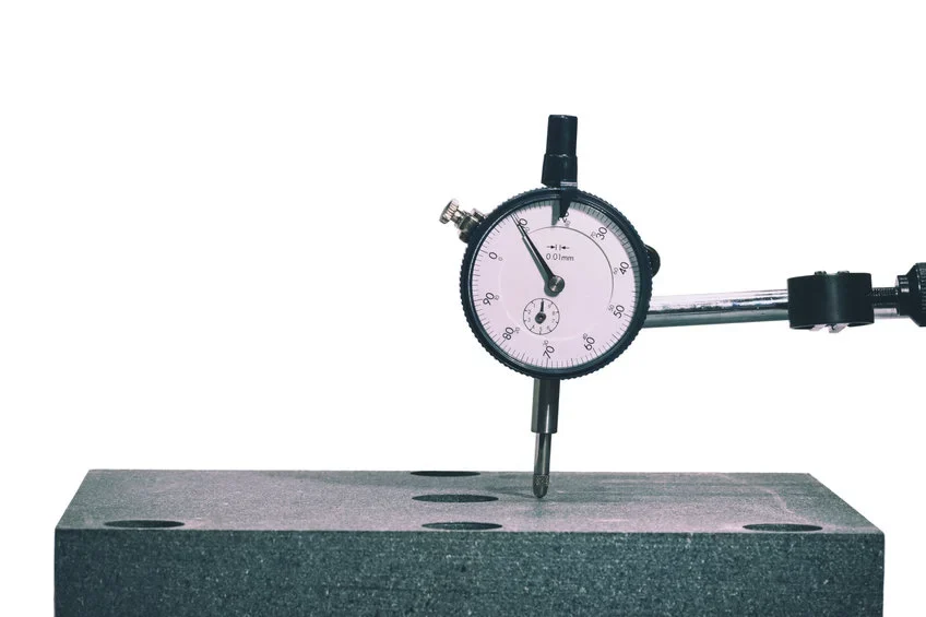 Dial indicator on granite surface plate measuring flatness and parallelism of graphite workpiece.
